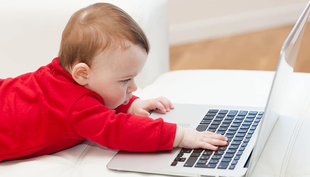 Eight months old baby girl using a laptop on the couch at home.