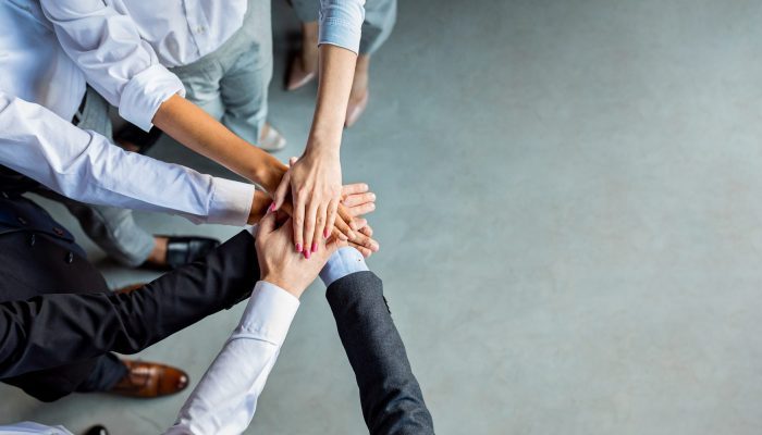 Teambuilding And Togetherness. Unrecognizable Business People Holding Hands Standing In Modern Office. Panorama, Above View, Empty Space